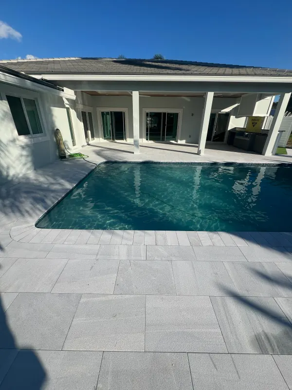Pool with a gray marble deck behind a covered patio