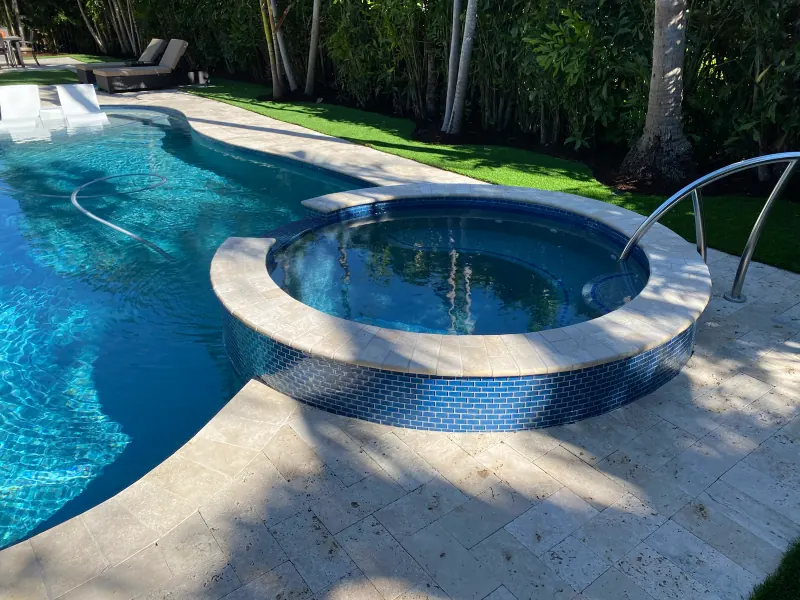 Freeform pool with a round raised spa and travertine deck