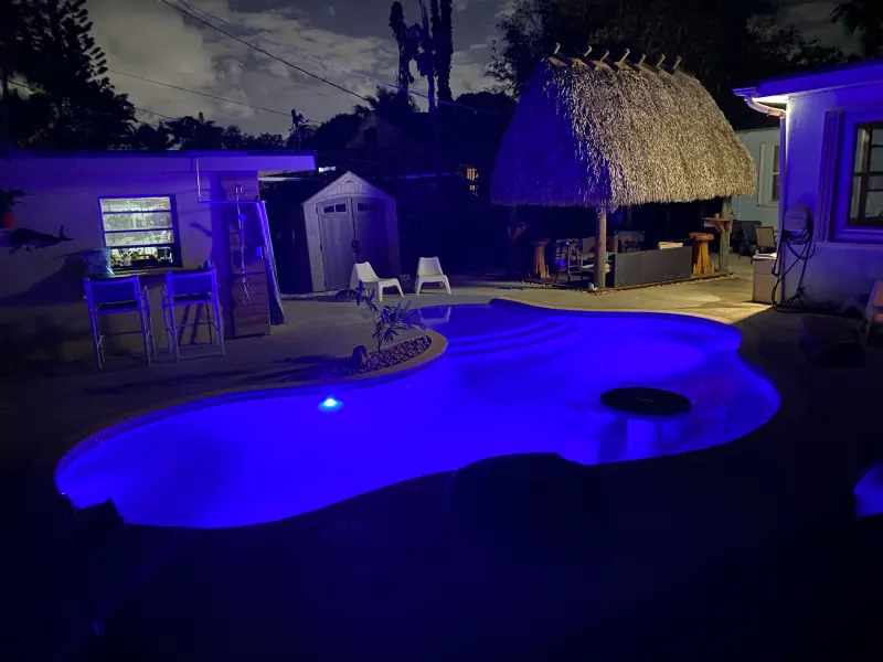 Freeform pool glowing blue at night beside a tiki hut