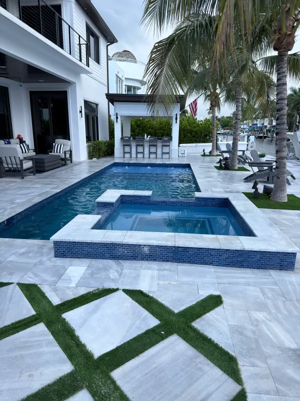 Pool with a raised spa, cabana bar and a marble deck laid in a turf grid