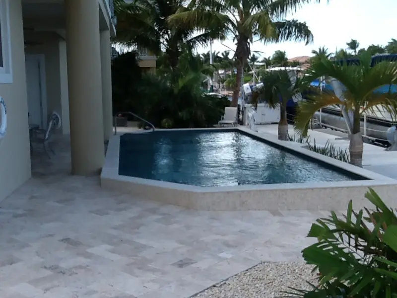 Geometric pool beside the house with a travertine deck