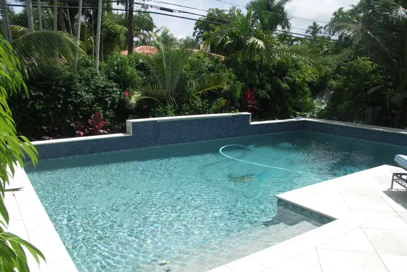 Pool with a raised glass-tile wall and white travertine deck